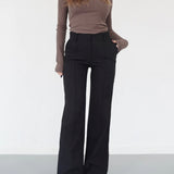Woman wearing high-waisted black wide-leg trousers with a ribbed brown top and white sneakers